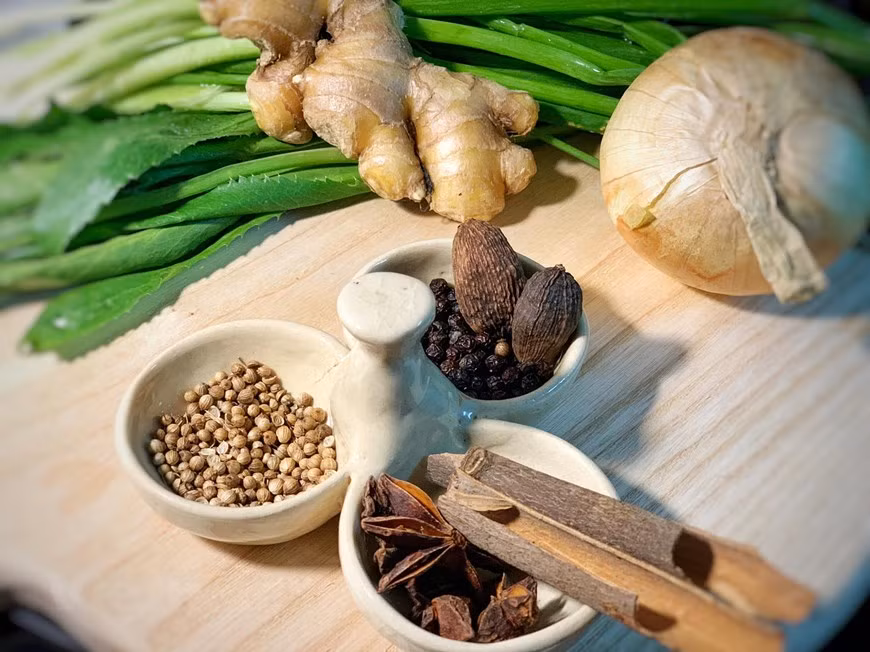 En cuanto a las especias para la deliciosa sopa vietnamita de ternera, más conocida como el Pho Bo, necesitas 5 unidades de anís estrellado, 2 canelas en rama, 5 clavos de olor, 1 cardamomo negro, 1/2 cucharada de semillas de cilantro, y 1/2 cucharada de semillas de hinojo. Cocinar al grill la cebolla, chalota, jengibre, canela y anís estrellado. Con la ayuda de un cuchillo quitar las partes más quemadas dejando un poquito. Reservar para luego. Tostar las especias. Ponerlas en una bolsita de infusión y reservar para luego. Mientras, en otra olla, hidratar los tallarines de arroz al menos durante 1 hora. (Fuente: VietnamPlus)