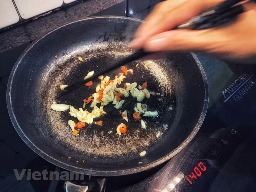 4. Saltear ajo y chili en aceite. Verter un poco de aceite de cocina en la sartén. Cuando esté caliente, agregar ajo y chili. No se debe cocinar demasiado (color amarillo), para evitar que se vuelva amargo muy rápido. Esta mezcla tendrá un aroma que despierta el apetito. En Vietnam, se usa el chili “de ojo de pájaro”, el tipo pequeñito pero muy picante. Este chili se cocina ampliamente para varios platos como sopas, ensaladas y platos salteados para dar el sabor pungente, el favorito de muchas personas. El ajo, igualmente, es un ingrediente indispensable de la gastronomía vietnamita. Se considera como sazón para los platos salteados o sofritos. 