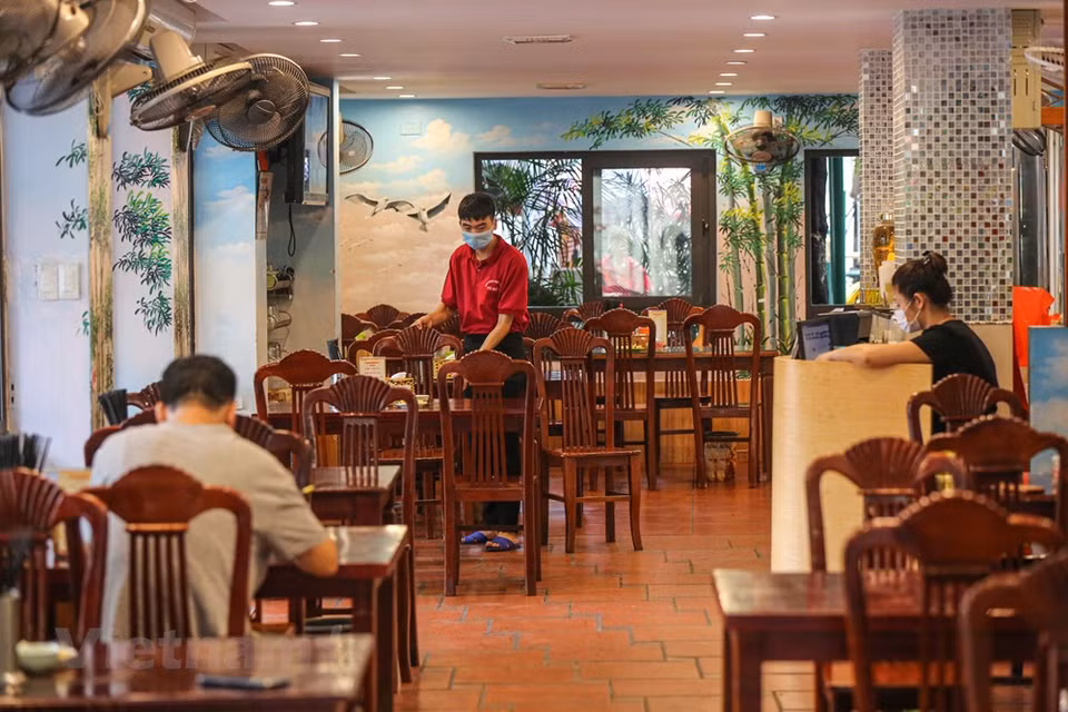 Los empleados en restaurantes deben usar mascarillas durante el servicio, realizar la medición de la temperatura corporal a los clientes y limpiar las superficies de los objetos de frecuente contacto. La Organización Mundial de la Salud (OMS) reconoció al COVID-19 como una pandemia global el 11 de marzo de 2020. El coronavirus se transmite generalmente de persona a persona a través de las pequeñas gotas de saliva, conocidas como microgotas de Flügge, que se emiten al hablar, estornudar, toser o espirar. Se difunde principalmente cuando las personas están en contacto cercano, pero también al tocar una superficie contaminada y luego llevar las manos contaminadas a la cara o partes del cuerpo con mucosa. Su período de incubación suele ser de cinco días, pero puede variar de dos a 14 días. (Foto: Minh Son / Vietnam +)