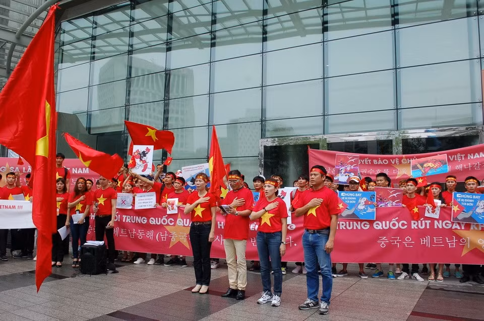 Los manifestantes cantan el himno vietnamita ante la bandera nacional (Fuente: VNA)