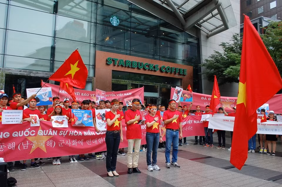 Los manifestantes cantan el himno vietnamita ante la bandera nacional (Fuente: VNA)