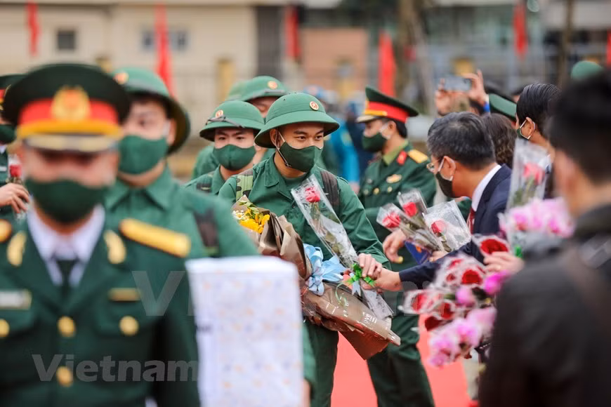 Con el fin de garantizar la seguridad sanitaria ante la situación del COVID-19, la ceremonia de entrega militar se lleva a cabo rápidamente. Los reclutas parten hacia su camino mientras reciben flores de las autoridades del distrito y altos funcionarios capitalinos. En 2021, la tasa de ciudadanos de la capital de Hanoi que cumplen con la orden de examen médico para el servicio militar obligatorio alcanzó el 100 por ciento. De los cuales, los pobladores elegibles con buena salud para el servicio militar fueron del 68,9 por ciento, mientras que aquellos con títulos universitarios y de secundaria profesional ocuparon el 43 por ciento, y los que escribieron solicitudes de voluntariado por sí mismos fueron del 30 por ciento del total. (Foto: Vietnam+)
