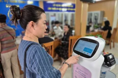 Ciudadana interactúa con un robot de IA que aplica tecnología de inteligencia artificial para ayudar en la realización de trámites administrativos en Hanoi. Foto: VNA