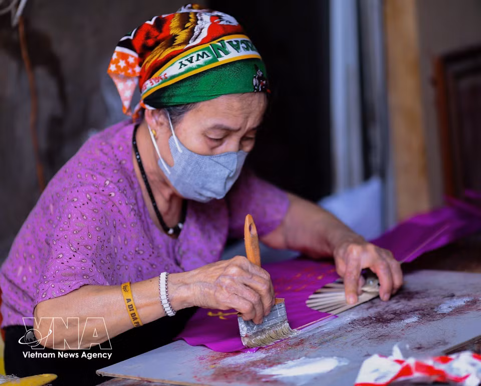 Con delicadeza, la artesana extiende el pegamento sobre cada capa de papel, preservando el espíritu artesanal que caracteriza a estos abanicos tradicionales. (Foto: VNA)