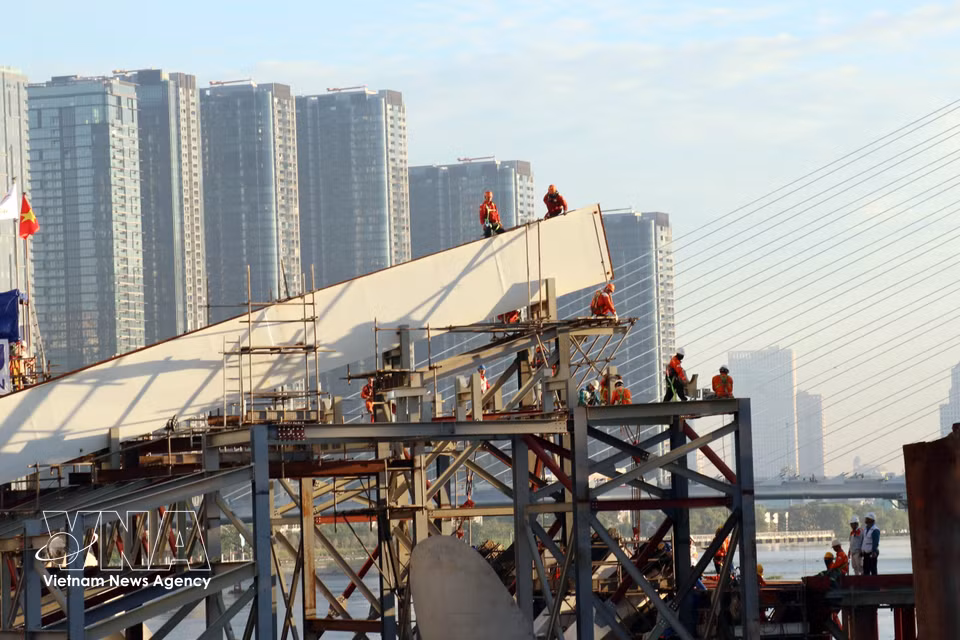Ingenieros y trabajadores en la obra preparan las operaciones para completar la unión de los tramos del puente peatonal sobre el río Saigón. Foto: VNA
