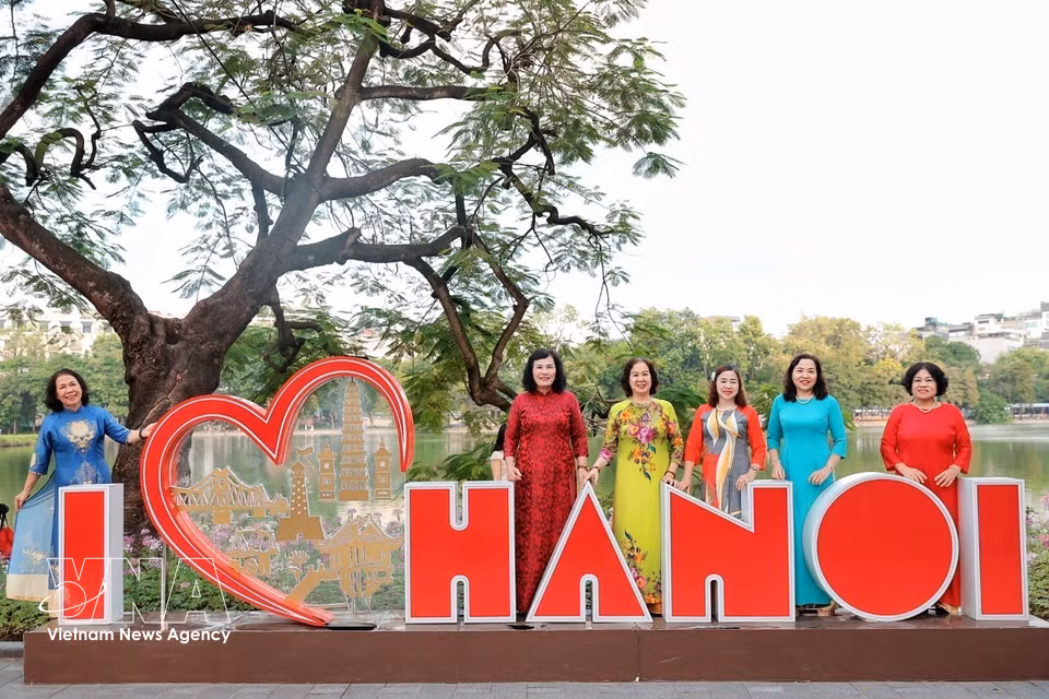 Mujeres mayores, ataviadas con el Ao dai (traje tradicional), disfrutan de una mañana otoñal y guardan el recuerdo de este momento. Foto: VNA