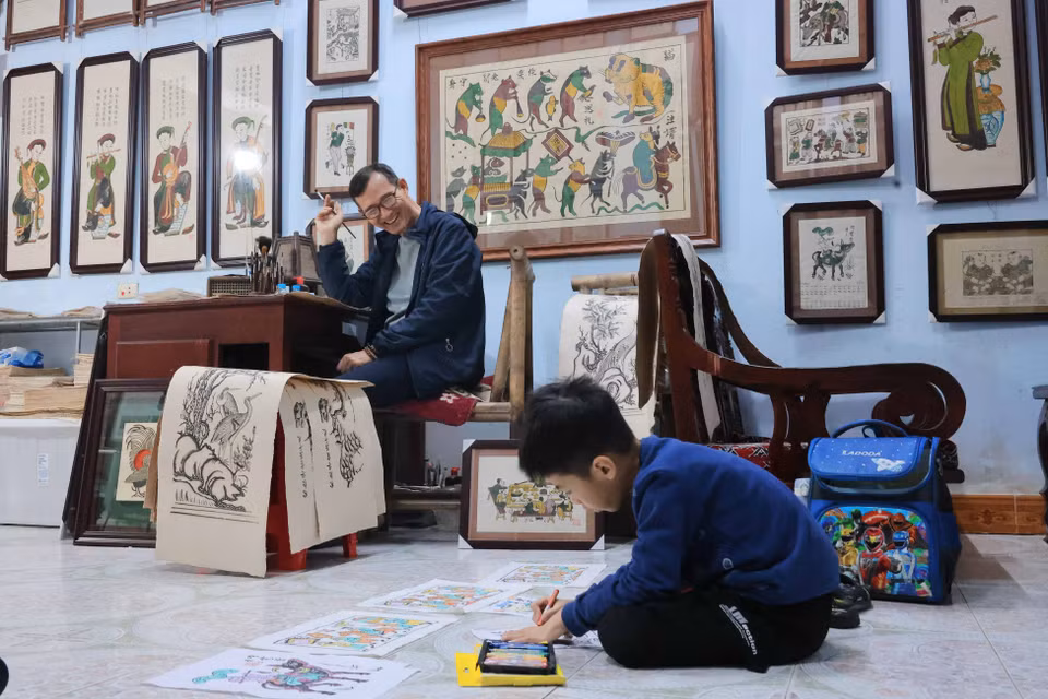 El reconocido artesano Nguyen Huu Qua, de la generación número 13 de pintores Dong Ho, disfruta ver a su nieto, Nguyen Huu Minh Dang, pintar sobre antiguos marcos Dong Ho. (Fuente: VNA)