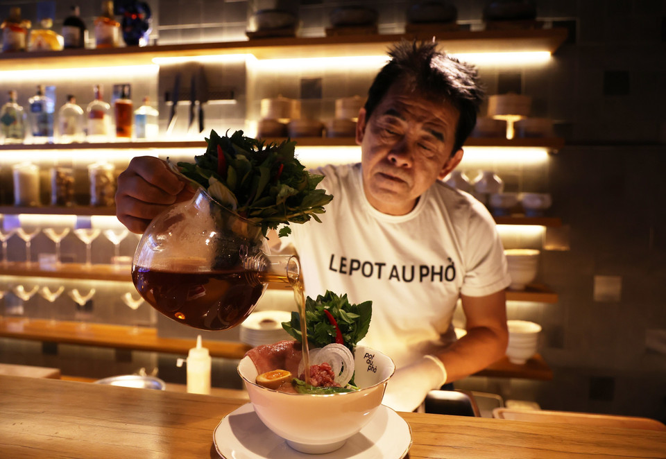 El chef Peter Cuong Franklin, propietario del restaurante Pot Au Pho, vierte caldo en un tazón especial de pho en el restaurante. (Foto: VNA)