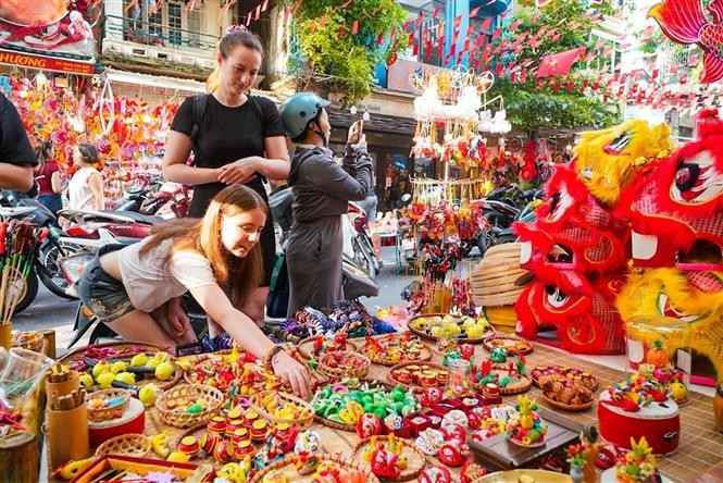 Las turistas extranjeras están interesadas ​​en conocer sobre los juguetes tradicionales vietnamitas del Festival del Medio Otoño. (Fuente: VNA)