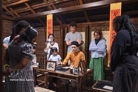 Los visitantes observan a un calígrafo realizar una demostración de caligrafía en un espacio de cultura tradicional durante el recorrido nocturno por el Templo de la Literatura en Hanoi. (Foto: VNA)
