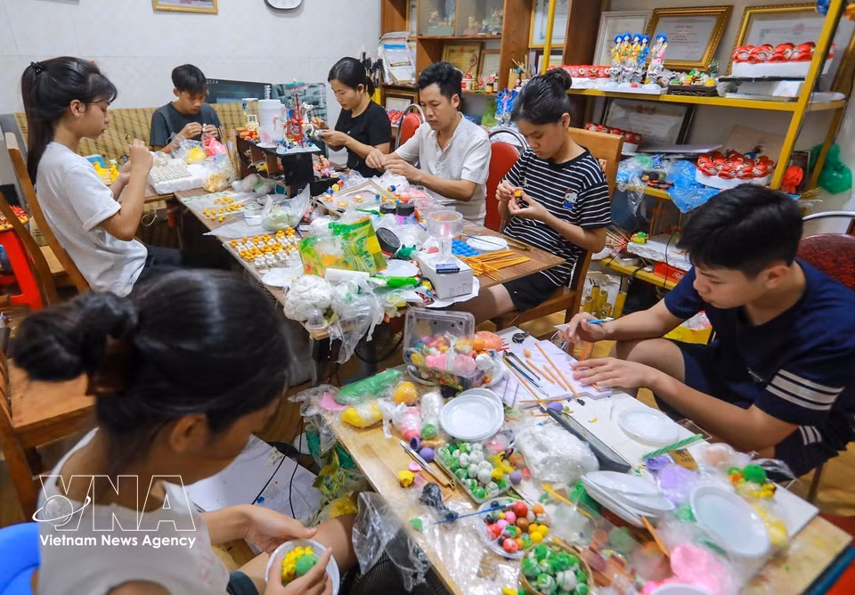 El artesano enseña y guía atentamente a jóvenes en la elaboración de obras de “to he”. Foto: Khanh Hoa – VNA