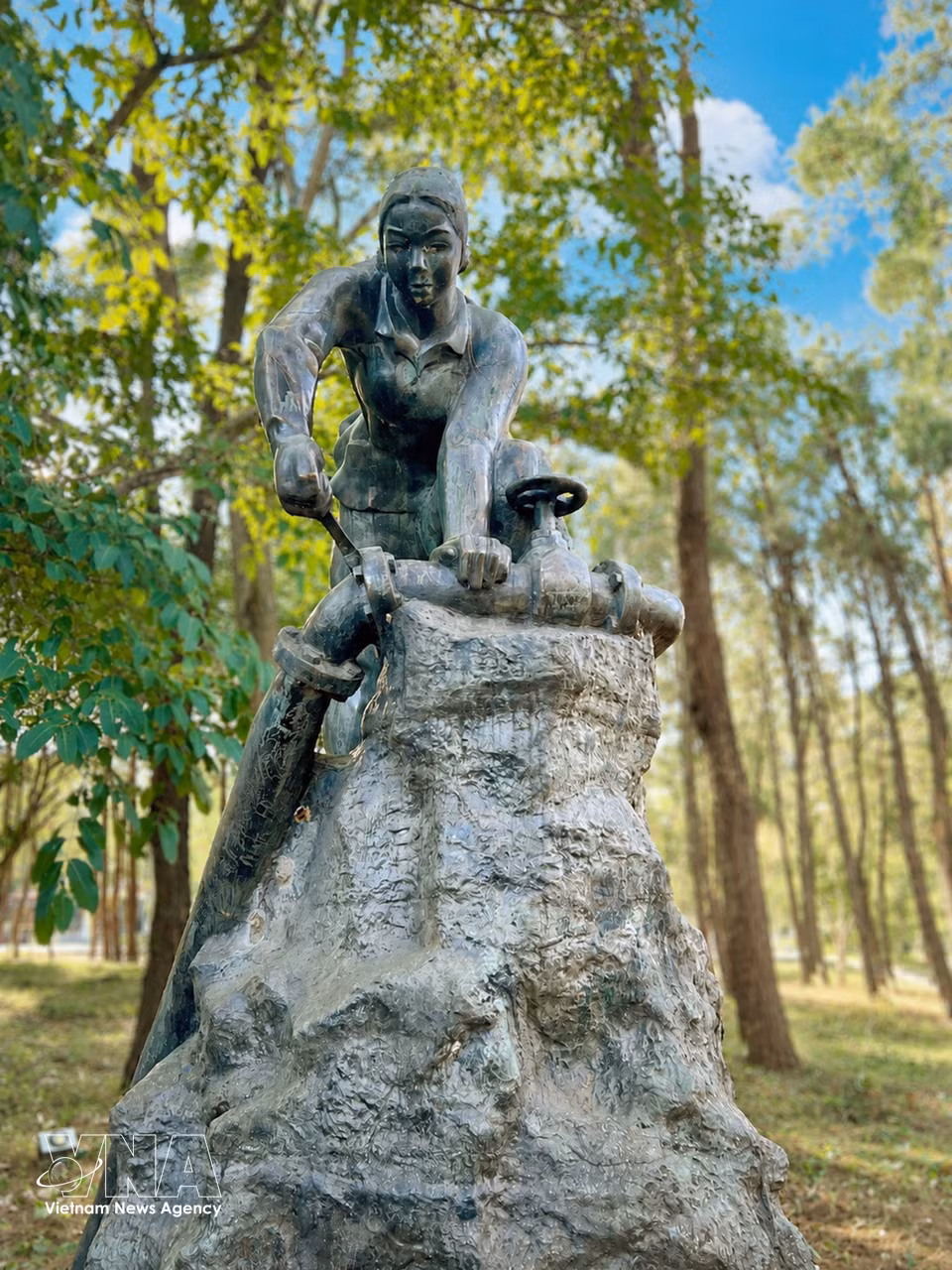 La estatua de bronce en el parque conmemorativo del cementerio representa la imagen de una joven reparando una tubería de combustible en medio del campo de batalla, evocando las contribuciones y sacrificios de las fuerzas logísticas en la legendaria ruta de Truong Son. Foto: Nguyen Linh – VNA