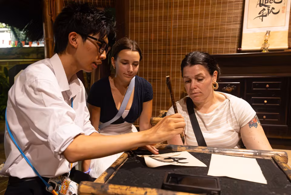 Turistas internacionales disfrutan de la experiencia del arte de la caligrafía con pincel bajo la guía de un promotor cultural. Foto: VNA