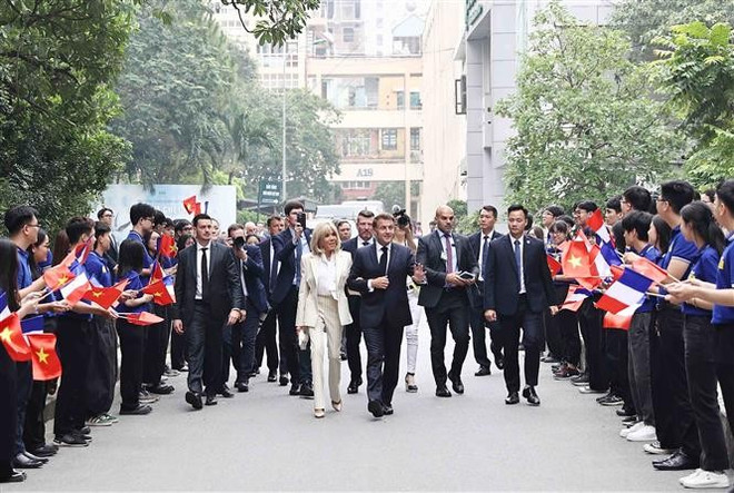 Estudiantes de la USTH dan la bienvenida al presidente francés, Emmanuel Macron, y a su esposa. (Foto: VNA) vna-potal-tong-thong-phap-va-phu-nhan-tham-truong-dai-hoc-khoa-hoc-va-cong-nghe-ha-noi-8057324.jpg