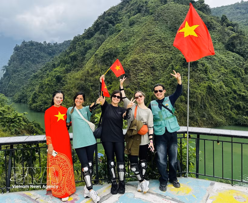 Turistas extranjeros se fotografían con entusiasmo junto a lugareños que visten trajes tradicionales adornados con la bandera roja y la estrella amarilla. (Foto: VNA)