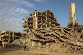 La gente camina entre los escombros de los edificios destruidos por el conflicto en la ciudad de Gaza. (Foto: Xinhua/VNA)