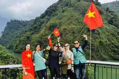 Turistas extranjeros se fotografían con entusiasmo junto a lugareños que visten trajes tradicionales adornados con la bandera roja y la estrella amarilla. (Foto: VNA)