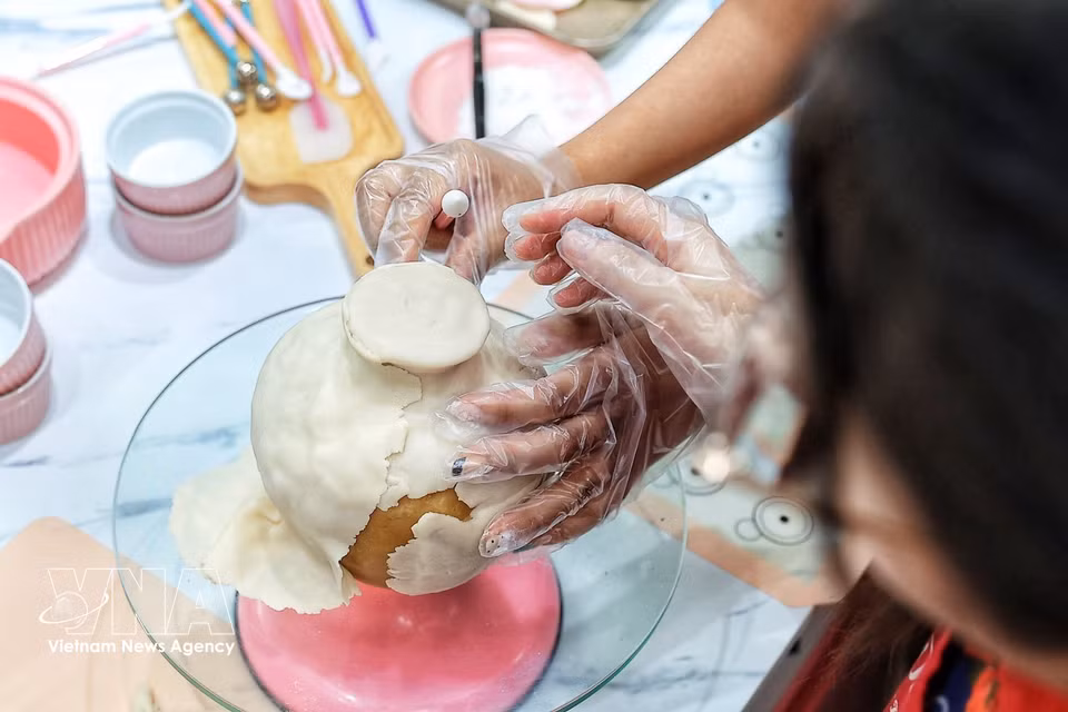 La artesana alisa y ajusta cuidadosamente cada parte de la masa que recubre el pastel de luna para dar forma al jarrón antes de decorarlo y combinarlo con las ramas florales de tò he. (Foto: VNA)