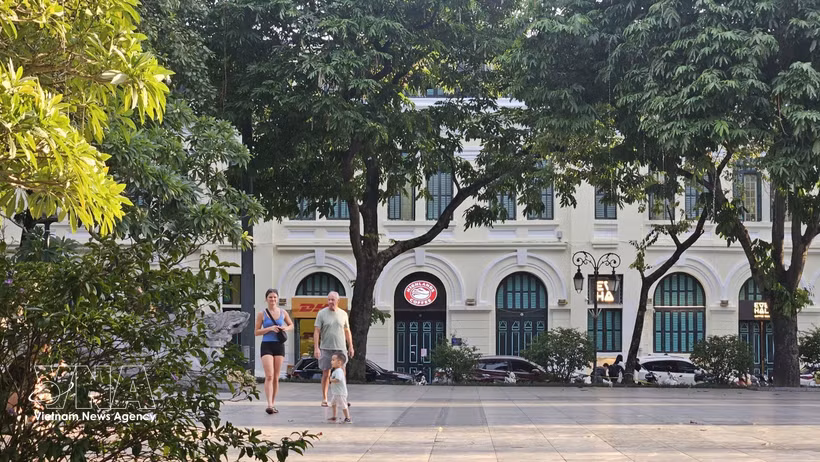Turistas extranjeros pasean bajo los árboles frondosos a orillas del lago Hoan Kiem, disfrutando del ambiente fresco de la capital. (Foto: VNA)