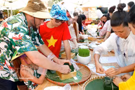 Los turistas experimentan la preparación de banh chung (paste redondo de arroz glutinoso). Foto: VNA)