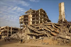 La gente camina entre los escombros de los edificios destruidos por el conflicto en la ciudad de Gaza. (Foto: Xinhua/VNA)