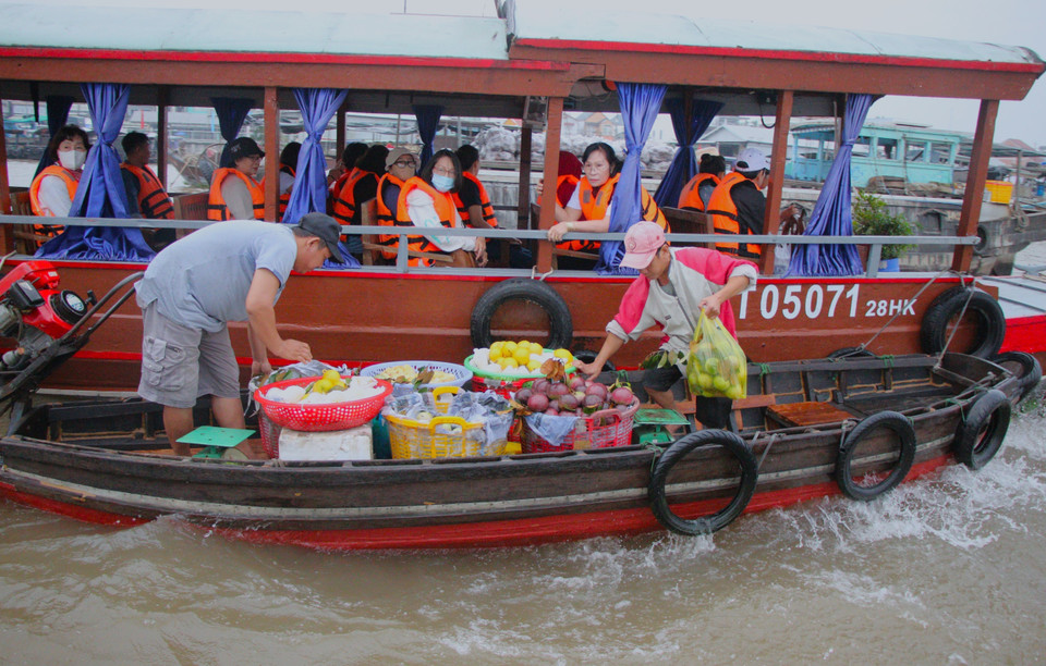 Turistas compran productos agrícolas durante su visita al mercado flotante de Cai Rang. Foto: VNA