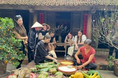 Los visitantes internacionales experimentan la envoltura de Banh Chung en la antigua aldea de Duong Lam. (Foto: VNA)