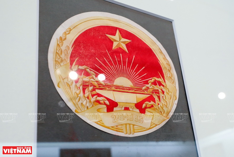 Un dibujo de boceto del escudo nacional de Vietnam del pintor Bui Trang Chuong con una estrella de cinco puntas sobre un fondo de bandera roja, el sol, las flores de arroz y el yunque que representa la industria.