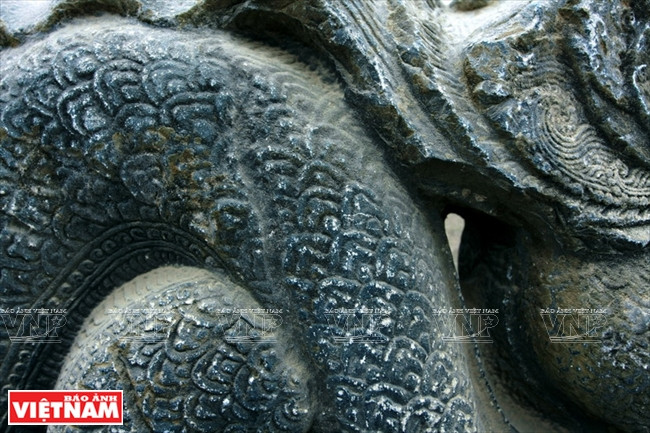 El par de dragones de piedra es tallado cuidadosamente, con sus cuerpos más pequeños abajo en sus colas, curvando en siete secciones, y totalmente cubierto con escamas. El dragón tiene cuatro pies, cada uno con tres clavos con pelos suaves. La cabeza ya no se ve, pero su larga melena sube y baja en nueve capas. Foto: Cong Dat