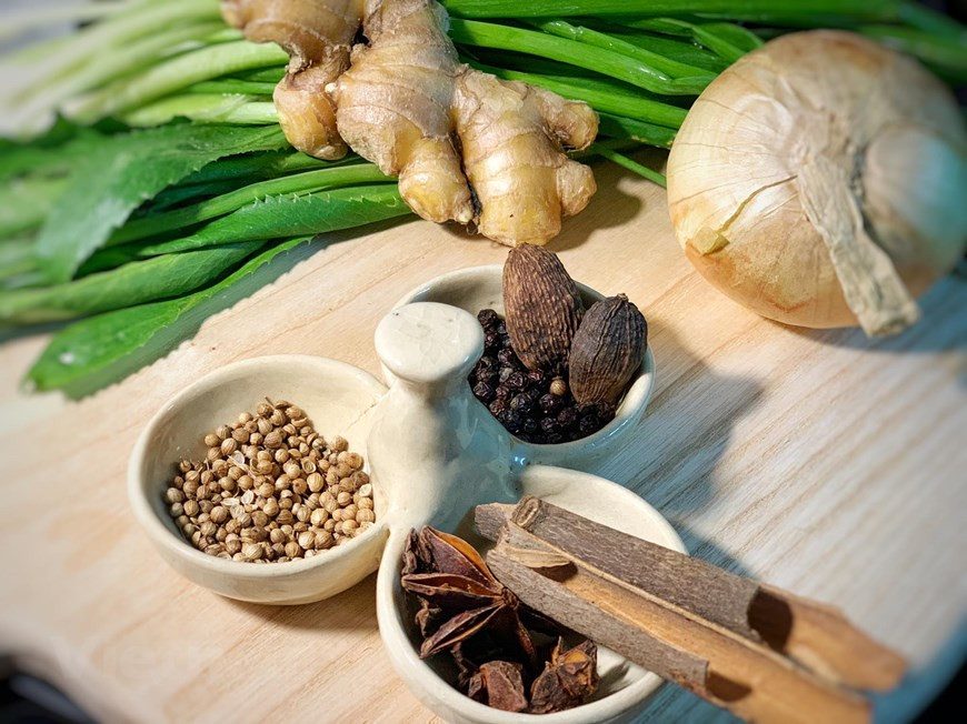 En cuanto a las especias para la deliciosa sopa vietnamita de ternera, más conocida como el Pho Bo, necesitas 5 unidades de anís estrellado, 2 canelas en rama, 5 clavos de olor, 1 cardamomo negro, 1/2 cucharada de semillas de cilantro, y 1/2 cucharada de semillas de hinojo. Cocinar al grill la cebolla, chalota, jengibre, canela y anís estrellado. Con la ayuda de un cuchillo quitar las partes más quemadas dejando un poquito. Reservar para luego. Tostar las especias. Ponerlas en una bolsita de infusión y reservar para luego. Mientras, en otra olla, hidratar los tallarines de arroz al menos durante 1 hora. (Fuente: VietnamPlus)