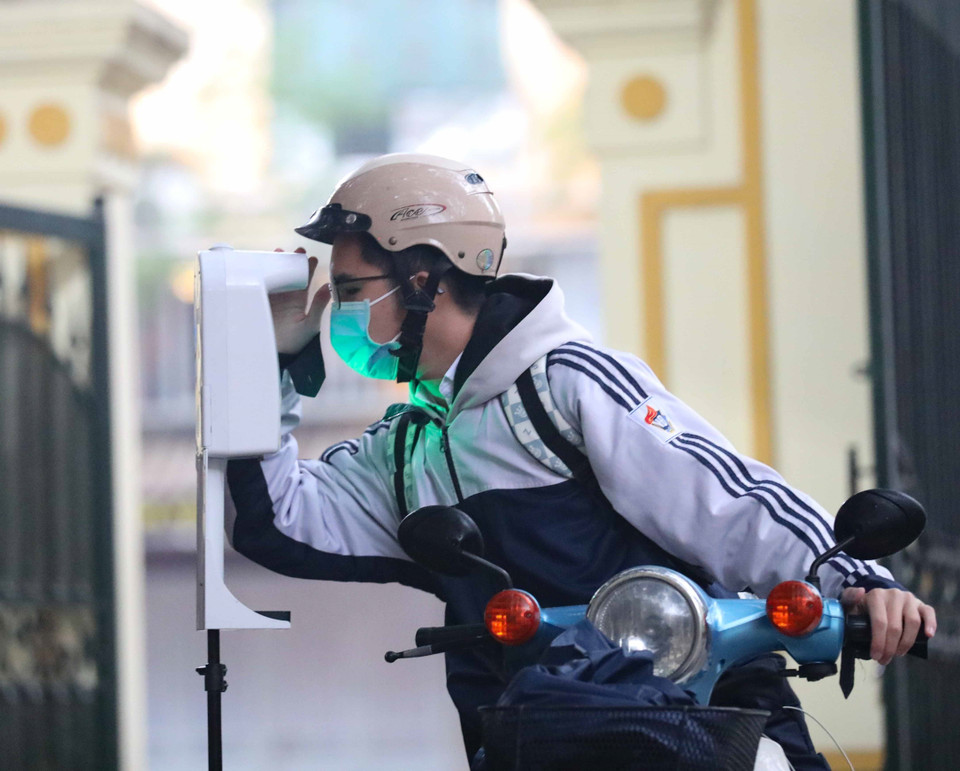 Los estudiantes se miden la temperatura corporal y desinfectan las manos antes de entrar a la escuela. (Foto: VNA)