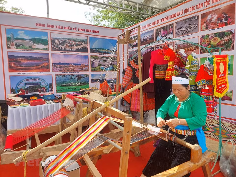 Demostración de habilidades de tejido de una mujer de la etnia Muong, procedente de la provincia de Hoa Binh. Los Muong han desarrollado una gran comunidad en la provincia de Hoa Binh, representando hasta el 63 por ciento de la población local. La vestimenta tradicional diaria de las niñas Muong es un pon (camisa corta), una blusa corta con una abertura en el pecho, mangas largas, de color marrón o blanca con una camisola en el interior. Se suele llevar un pañuelo blanco y azul. La falda es una negra cerrada. Como característica distintiva de los trajes de Muong sobresalen los patrones emergentes entre el vestido y la pretina y la cintura (Fuente: Vietnam +)