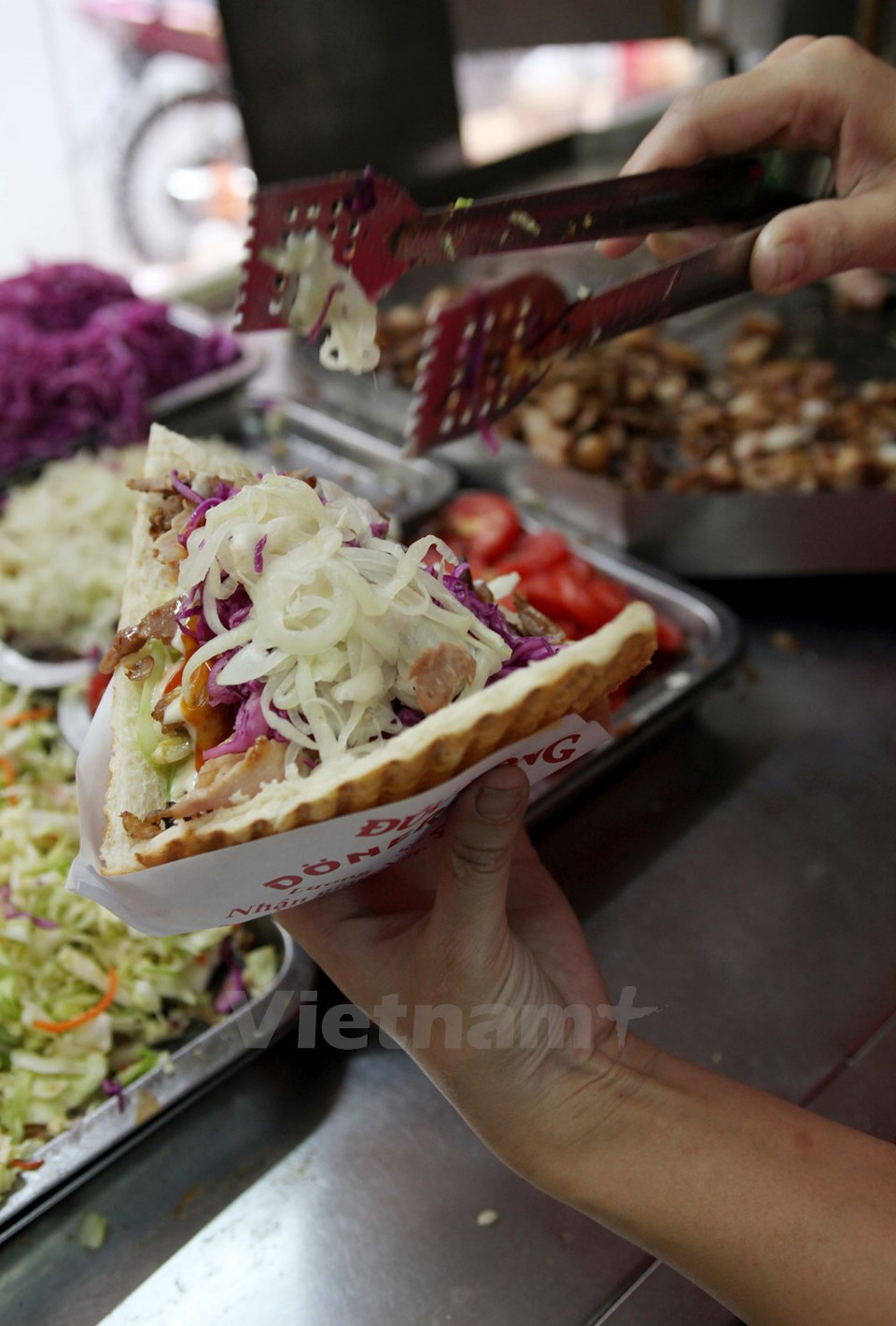 Se rellena el pan con carne y se lo aplasta en una máquina térmica. La ensalada acompañante incluye pepino, tomate, cebolla y col morada ácidos y dulces. 