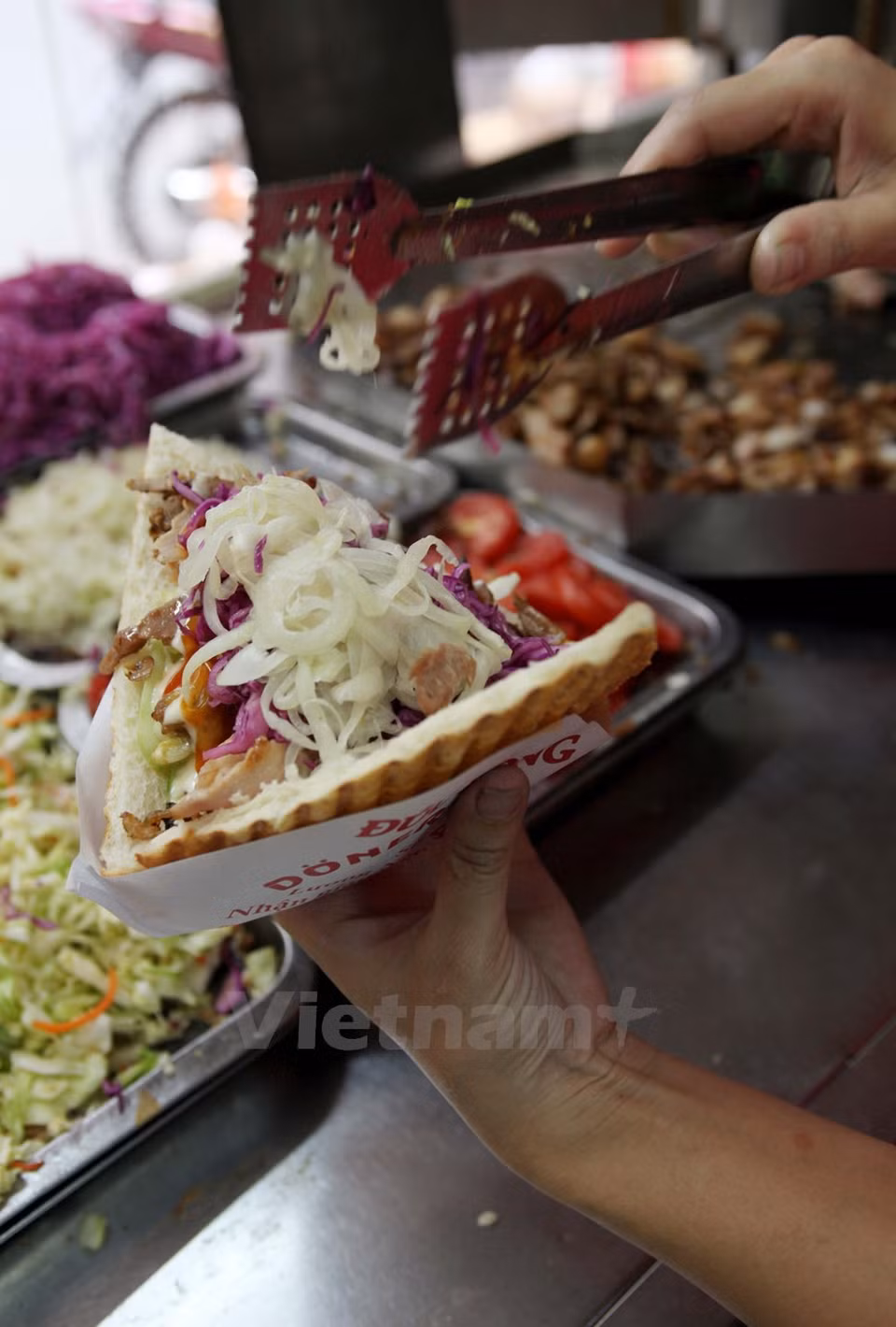 Se rellena el pan con carne y se lo aplasta en una máquina térmica. La ensalada acompañante incluye pepino, tomate, cebolla y col morada ácidos y dulces. 