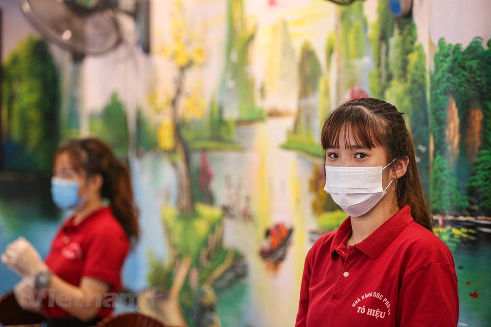 Todos los empleados en los restaurantes deben usar mascarillas para atender a los clientes e implementar drásticamente las medidas destinadas a prevenir la propagación epidémica de COVID-19. La Organización Mundial de la Salud (OMS) la reconoció como una pandemia global el 11 de marzo de 2020. El coronavirus se transmite generalmente de persona a persona a través de las pequeñas gotas de saliva, conocidas como microgotas de Flügge, que se emiten al hablar, estornudar, toser o espirar. Se difunde principalmente cuando las personas están en contacto cercano, pero también se puede trasmitir al tocar una superficie contaminada y luego llevar las manos contaminadas a la cara o partes del cuerpo con mucosa. Su período de incubación suele ser de cinco días, pero puede variar de dos a 14 días. (Foto: Minh Son / Vietnam +)