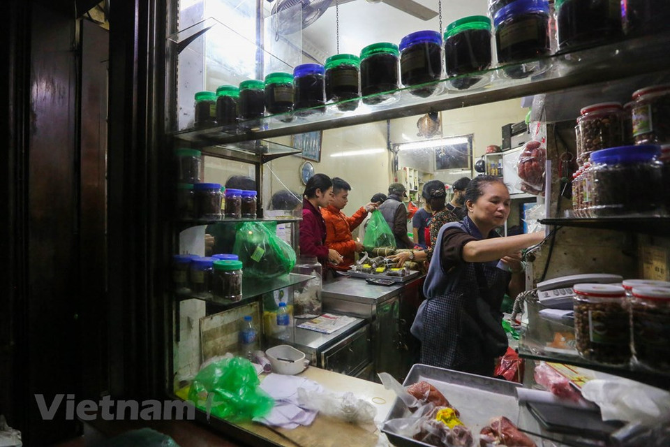 Dentro de la tienda, la propietaria Nguyen Thi Chan y sus empleados entregan Banh Chung (pasteles cuadrados de arroz glutinoso, cerdo y guisantes envueltos en hojas de banano) y Gio Cha (jamón o salchicha de Vietnam) para los clientes. Considerado un elemento esencial del altar familiar con motivo del Tet, la elaboración y consumo de Banh Chung durante esa época es una tradición bien conservada por los vietnamitas. Debido a su larga historia y duradera popularidad, el bánh chưng se considera uno de los platos nacionales junto al Nem Ran y el Pho , Fuente: Minh Son / Vietnam +)