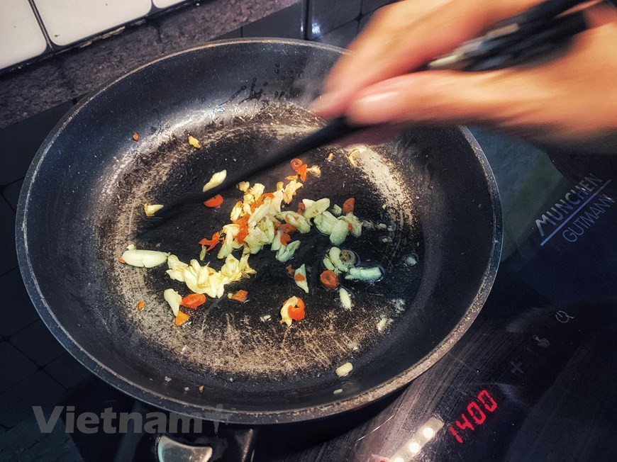 4. Saltear ajo y chili en aceite. Verter un poco de aceite de cocina en la sartén. Cuando esté caliente, agregar ajo y chili. No se debe cocinar demasiado (color amarillo), para evitar que se vuelva amargo muy rápido. Esta mezcla tendrá un aroma que despierta el apetito. En Vietnam, se usa el chili “de ojo de pájaro”, el tipo pequeñito pero muy picante. Este chili se cocina ampliamente para varios platos como sopas, ensaladas y platos salteados para dar el sabor pungente, el favorito de muchas personas. El ajo, igualmente, es un ingrediente indispensable de la gastronomía vietnamita. Se considera como sazón para los platos salteados o sofritos.