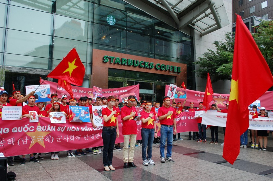 Los manifestantes cantan el himno vietnamita ante la bandera nacional (Fuente: VNA)