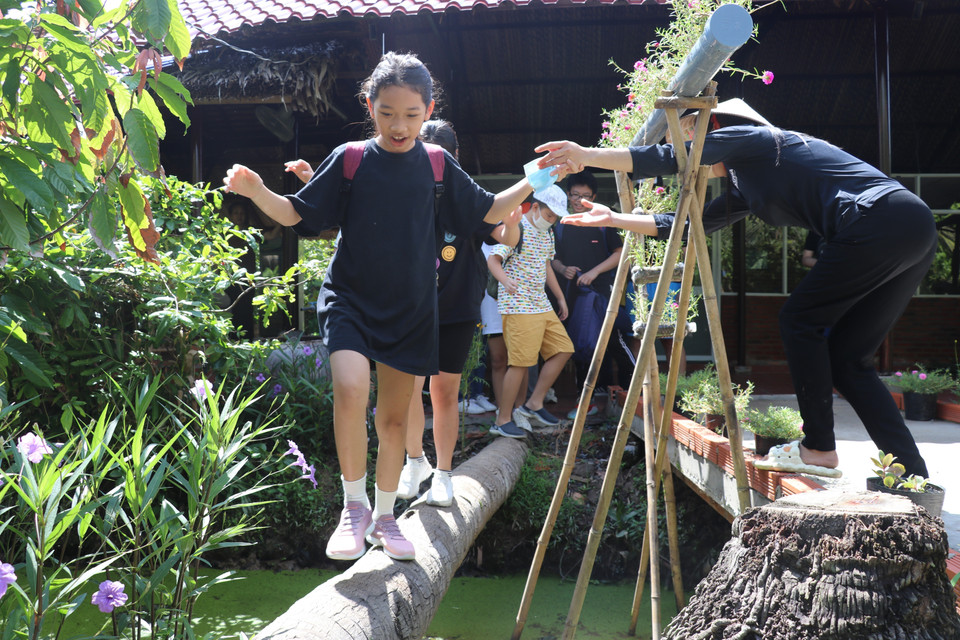 Jóvenes disfrutan de la experiencia de caminar sobre un puente de cocos en el huerto. Foto: VNA