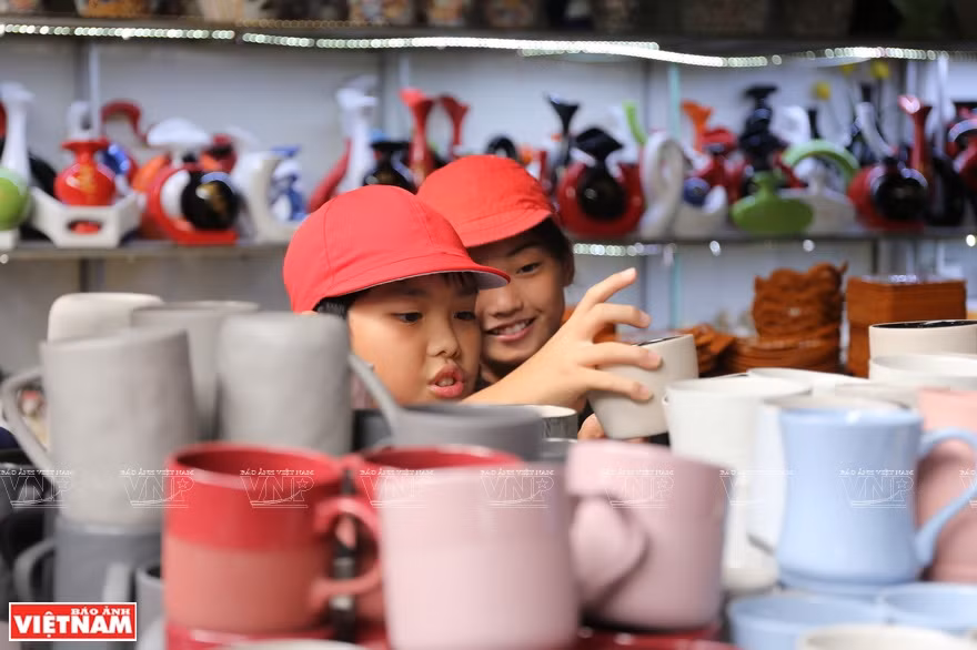 Dos niños procedentes de Japón seleccionan los vasos preciosos en el mercado de cerámica de Bat Trang, durante una acampada organizada por su escuela. (Fuente: VNA)