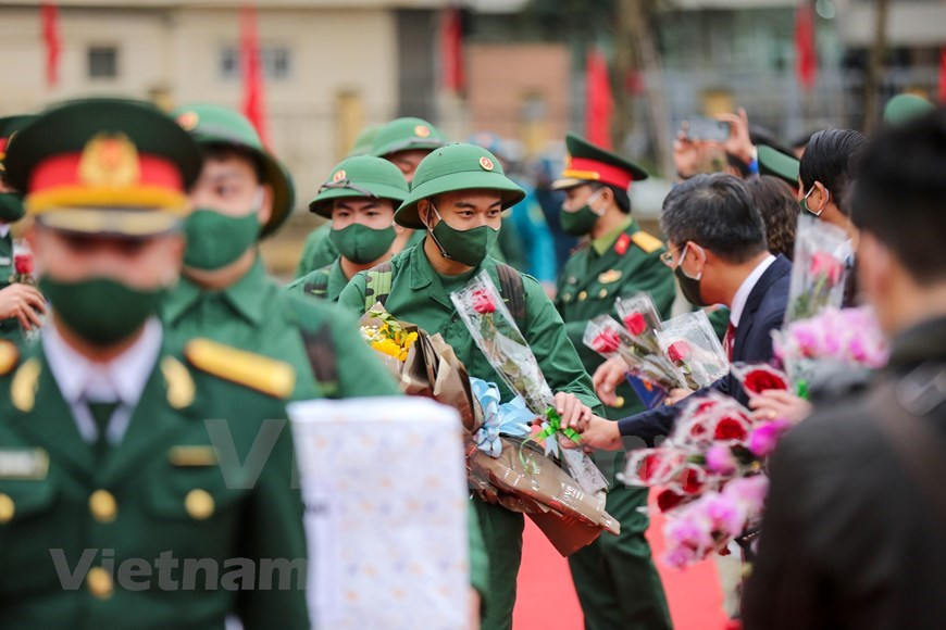 Con el fin de garantizar la seguridad sanitaria ante la situación del COVID-19, la ceremonia de entrega militar se lleva a cabo rápidamente. Los reclutas parten hacia su camino mientras reciben flores de las autoridades del distrito y altos funcionarios capitalinos. En 2021, la tasa de ciudadanos de la capital de Hanoi que cumplen con la orden de examen médico para el servicio militar obligatorio alcanzó el 100 por ciento. De los cuales, los pobladores elegibles con buena salud para el servicio militar fueron del 68,9 por ciento, mientras que aquellos con títulos universitarios y de secundaria profesional ocuparon el 43 por ciento, y los que escribieron solicitudes de voluntariado por sí mismos fueron del 30 por ciento del total. (Foto: Vietnam+)