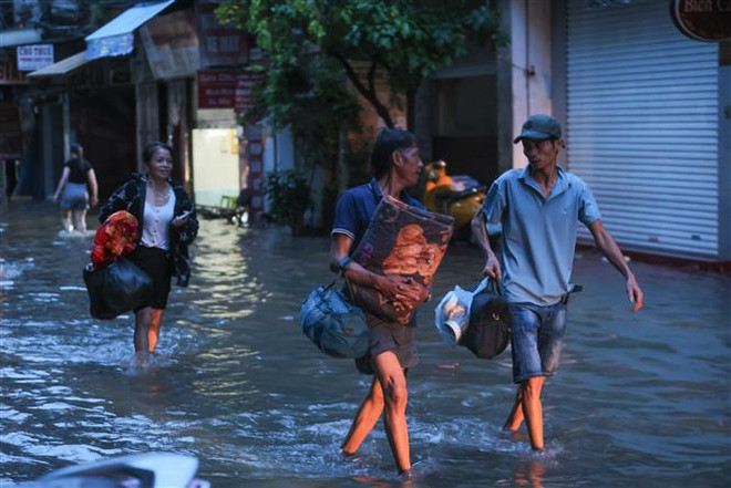 Residentes de la calle de Cau Dat, distrito de Hoan Kiem, se alejan de la zona inundada. (Fuente:VNA) flooding.jpg