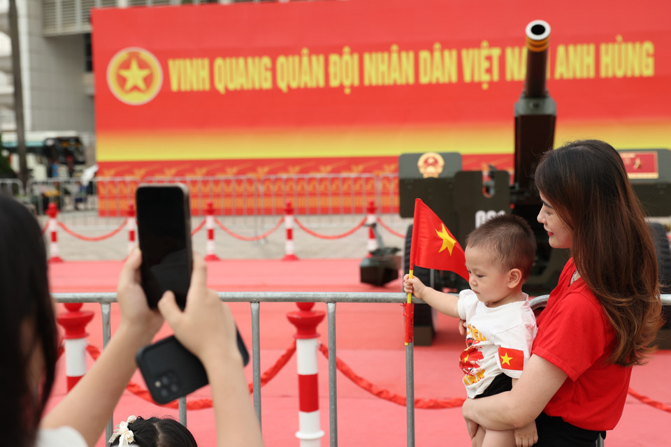 Los padres permiten a sus niños portar la bandera nacional para tomarse fotos con la artillería ceremonial. Foto: VNA