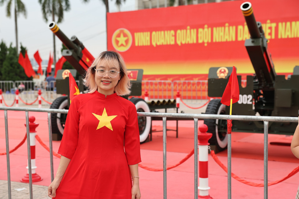 Una joven con un traje tradicional con el motivo de la bandera nacional, sonriendo junto a las baterías de artillería. Foto: VNA