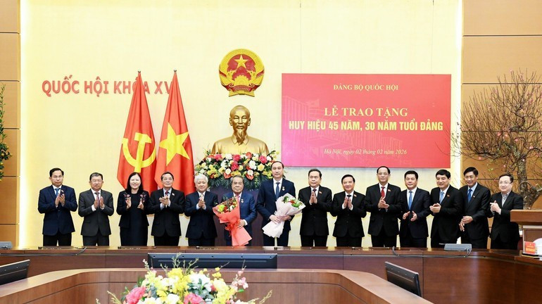 El presidente de la Asamblea Nacional, Tran Thanh Man, y funcionarios felicitan a Duong Thanh Binh y Phung Khanh Tai (con flores) por la concesión de las insignias de 45 y 30 años de membresía del Partido. (Foto: nhandan.vn)