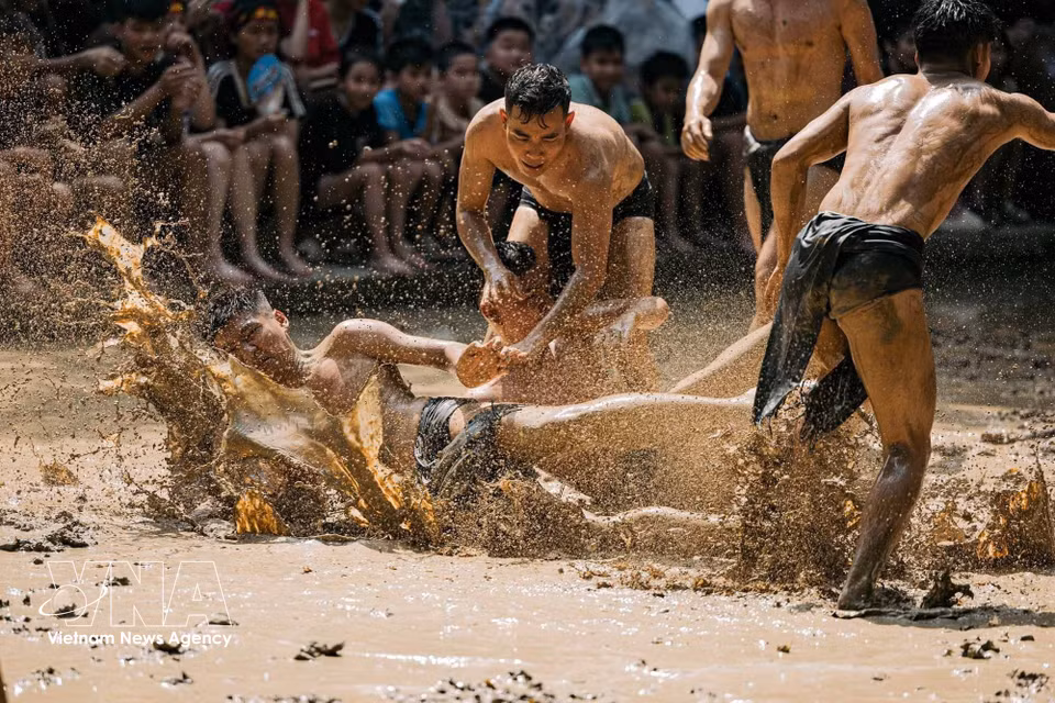 Un jugador cae en el campo de barro tras un fuerte choque, mientras sus compañeros y los rivales continúan persiguiendo la trayectoria de la bola. Foto: VNA