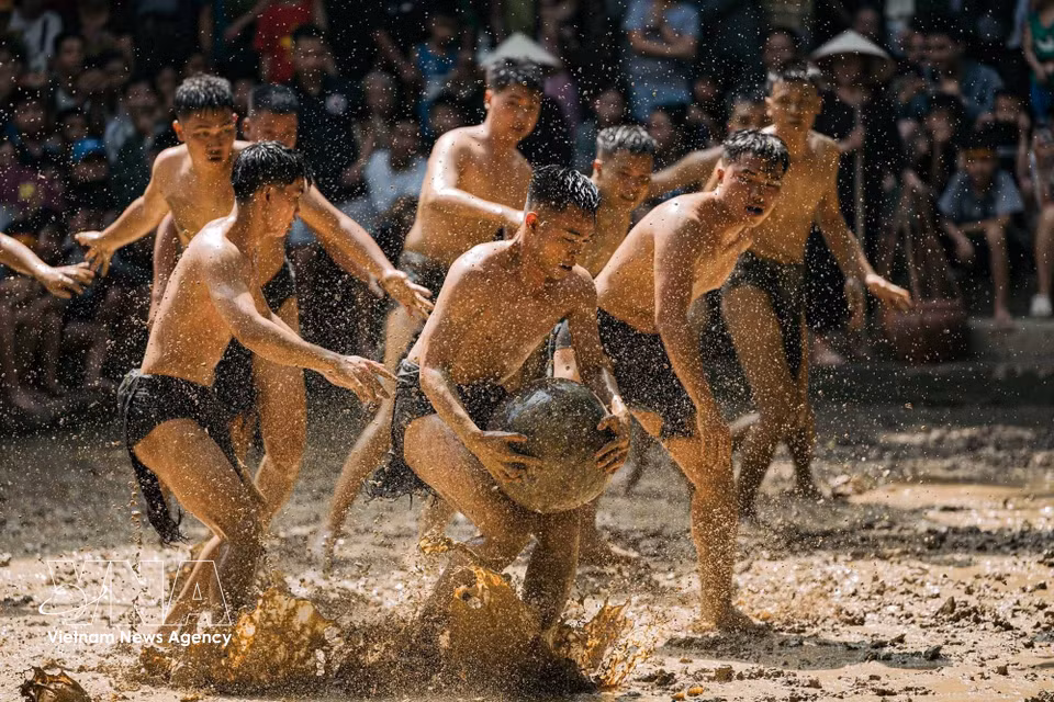 Un jugador se agacha, sujetando firmemente la bola entre el barro y el agua salpicada, mientras compañeros y rivales se acercan. Cada avance hacia el hoyo de puntuación implica un intenso forcejeo en el campo. Foto: VNA