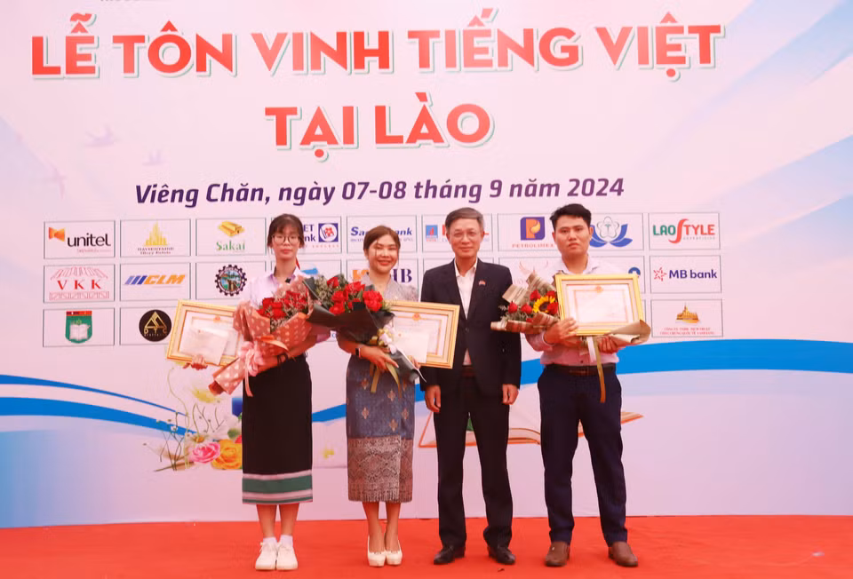 El encargado de negocios de Vietnam en Laos, Phan Minh Chien, entrega certificados de mérito y premios a tres concursantes que participan en la ronda final del concurso "En busca de embajadores vietnamitas en el extranjero en 2024". (Fuente: VNA)