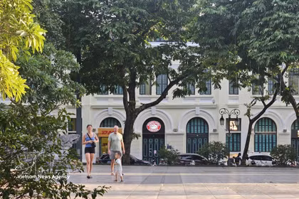 Turistas extranjeros pasean bajo los árboles frondosos a orillas del lago Hoan Kiem, disfrutando del ambiente fresco de la capital. (Foto: VNA)