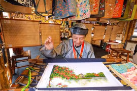 Una artesana borda una pintura en el área de la exposición. (Foto: VNA)
